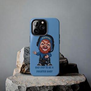 Könnte beinhalten: Eine blaue iPhone-Hülle mit einer Cartoon-Illustration einer Person mit Bart und Mikrofon. Der Text "Bad day to be a doubter baby" ist auf der Hülle aufgedruckt.