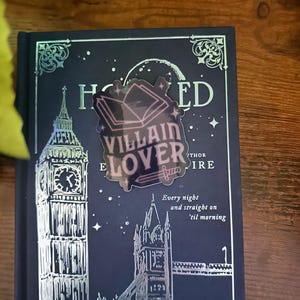 Puede incluir: Una pegatina hologr&aacute;fica con un dise&ntilde;o de libro y el texto "VILLAIN LOVER" en una cubierta de libro azul oscuro con un dise&ntilde;o en relieve plateado del Tower Bridge y el Big Ben. La cubierta del libro tambi&eacute;n tiene el texto "Every night and straight on 'til morning".