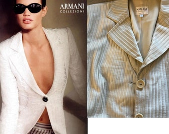Puede incluir: Una chaqueta blanca con cuello en V profundo y dos botones. La chaqueta está hecha de una tela texturizada y tiene un patrón a rayas. La etiqueta en la chaqueta dice "ARMANI COLLEZIONI".