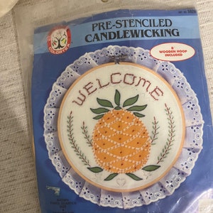 May include: A pre-stenciled candlewicking kit featuring a welcome sign with a pineapple design. The kit includes an 8-inch wooden hoop and is shown in a three-quarter size.