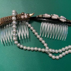 Puede incluir: Dos peines para el cabello con detalles de perlas y oro. Los peines están unidos a un collar de perlas.