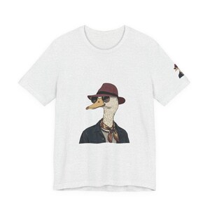Peut inclure: T-shirt gris clair avec un canard de dessin animé portant un fedora bordeaux, des lunettes de soleil, une écharpe rayée et une veste noire. Le canard est une illustration fantaisiste, idéale pour les tenues décontractées.
