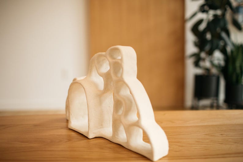 May include: A cream-colored ceramic sculpture featuring an organic, porous structure with multiple rounded openings and a smooth, matte finish. The object has a curved, asymmetrical silhouette with interconnected hollow sections throughout its form.