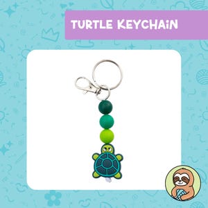 May include: A green and blue turtle keychain with a silver key ring and green and blue beads. The turtle has a small, black eye and a white mouth.