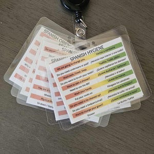 May include: A retractable badge reel with several laminated cards. The cards have text in English and Spanish related to hygiene and patient care. The cards are in a clear plastic holder and are attached to a black badge reel.