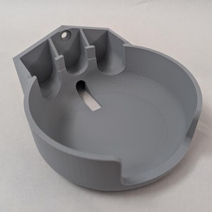 May include: A gray 3D printed wall mount for a smart speaker. The mount has a circular opening for the speaker and a slot for the power cord.