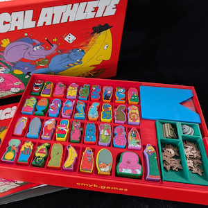 May include: A red board game box with the title "MAGICAL ATHLETE" and a cartoon illustration of a banana and other characters. The game box contains colorful game pieces and accessories. The game pieces are in various shapes and colors.