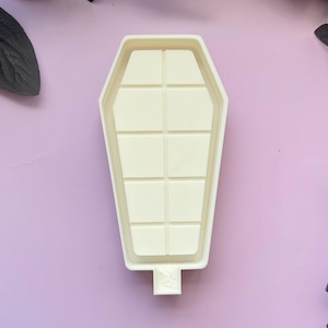 May include: White coffin-shaped silicone mold with a grid pattern inside. The mold is designed for making resin crafts.