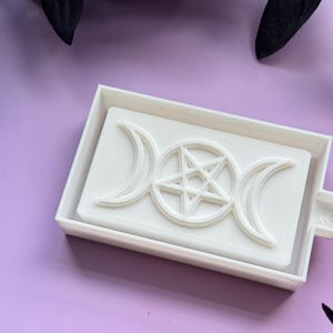 May include: White plastic mold for making soap or resin. The mold features a raised design of a pentacle and triple moon symbol.