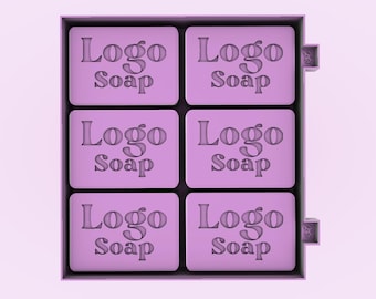 May include: A box of six lavender-colored soaps, each with the words "Logo Soap" embossed on the surface. The soaps are rectangular and neatly arranged within a dark gray box, set against a light purple background.