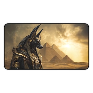 May include: A rectangular mouse mat featuring an illustration of Anubis, the Egyptian god of the afterlife, with the pyramids in the background. The artwork is rendered in shades of gold, black, and brown, with a dramatic sky.