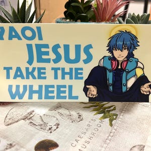 Może przedstawiać: Prostokątny znak z napisem "YAOI JESUS TAKE THE WHEEL" w kolorze niebieskim. Postać w stylu anime z niebieskimi włosami i słuchawkami znajduje się po prawej stronie znaku. Tło jest jasnożółte.