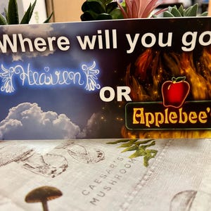 Puede incluir: Una tarjeta con el texto "Where will you go?" encima de las opciones "Heaven" y "Applebee's". El texto "Heaven" está en una fuente azul brillante con alas de ángel. El texto "Applebee's" está en un letrero verde y dorado con una manzana roja.