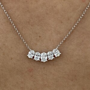 Könnte beinhalten: Eine zarte Silberkette mit fünf oval geschliffenen Diamanten, die in einer geschwungenen Anordnung angeordnet sind. Die Diamanten funkeln auf der Haut und erzeugen einen klassischen und eleganten Look. Die Kette ist fein und mit Gliedern versehen.