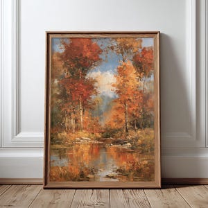 May include: A framed landscape painting depicting an autumn forest scene with vibrant red and orange trees reflected in a calm body of water. The artwork features a soft blue sky visible through the canopy, captured in a wooden frame.