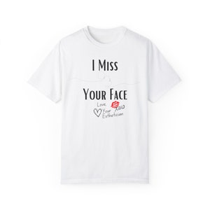 Puede incluir: Camiseta blanca con el texto "I Miss Your Face" y una marca de beso de lápiz labial rojo. Debajo del texto hay un corazón y las palabras "Love, Your Esthetician" y "xoxo".
