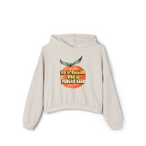 Może przedstawiać: Jasnobeżowa bluza z kapturem z grafiką brzoskwini i tekstem "My Brazilian Wax is Peachy Keen" w retro czcionce.