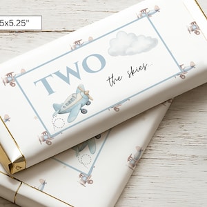 May include: Two wrapped candy bars with a white background and gold edges. The bars are decorated with a light blue frame, airplanes, and a cloud. The text "TWO the skies..." is printed on the front. The bars measure 5.5 x 5.25 inches.