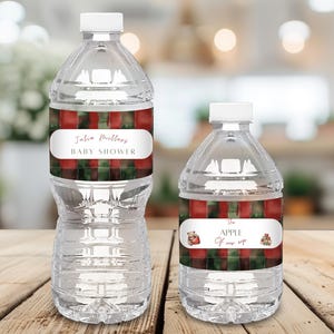 Op de afbeelding: Twee doorzichtige plastic waterflessen met witte doppen. De grotere fles heeft een etiket met de tekst "Julia Mullers BABY SHOWER". De kleinere fles heeft een etiket met de tekst "The APPLE Of our eye". De etiketten hebben een rood-groen ruitpatroon.