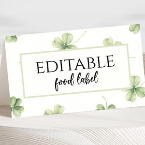 May include: A folded, rectangular food label with the words "EDITABLE food label" in black script. The label is white with a light green border and watercolor shamrock accents. The label is displayed on a white surface.