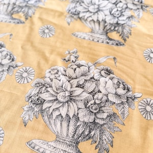 May include: A mustard yellow fabric featuring a repeating black and white line art pattern of floral arrangements in ornate urns. The design includes detailed sketches of various flowers and small circular blossoms scattered across the surface.