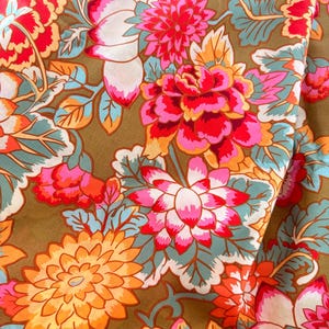 May include: A fabric featuring a dense floral pattern with large, vibrant blossoms in shades of hot pink, orange, and red. The flowers are set against a muted olive green background, accented by light blue leaves and stems throughout the design.