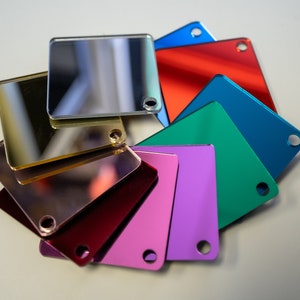 May include: A set of eight square mirror tiles in various colors, including gold, silver, red, blue, green, and purple. Each tile has a small hole in the corner.