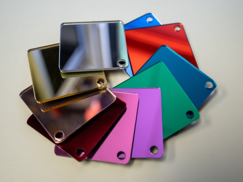May include: A set of eight square mirror tiles in various colors, including gold, silver, red, blue, green, and purple. Each tile has a small hole in the corner.