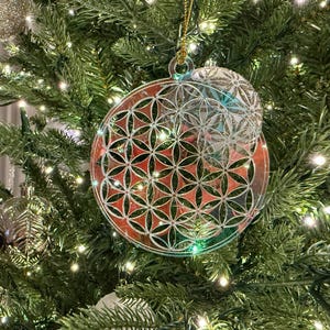 May include: A clear, round Christmas ornament with a red and silver floral design, hanging on a green Christmas tree. The ornament has a smaller, matching sphere attached. The tree is decorated with lights and other ornaments.
