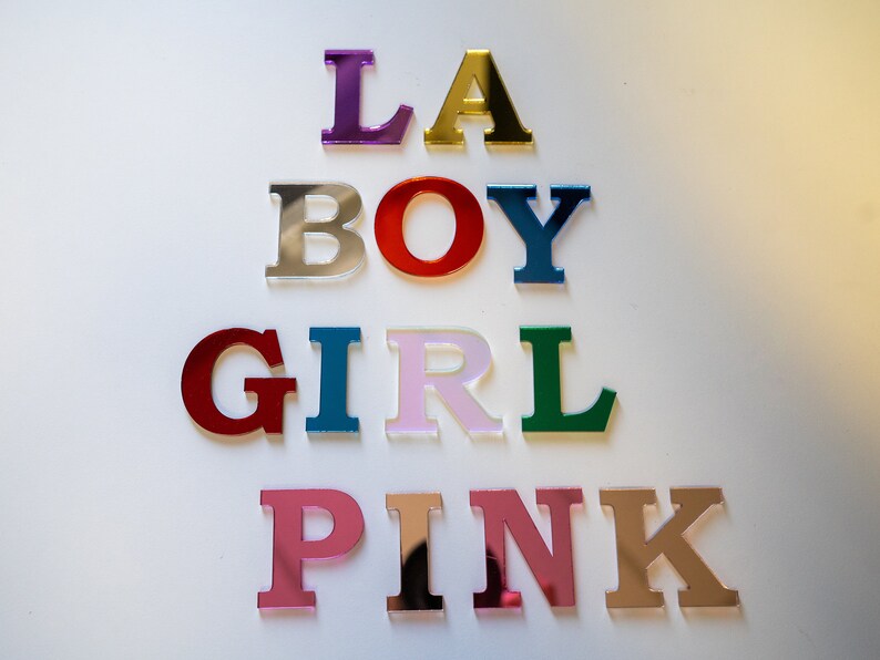May include: Colorful acrylic letters spelling out the words "LA BOY GIRL PINK". The letters are arranged in a pyramid shape, with the largest letters at the top and the smallest letters at the bottom.
