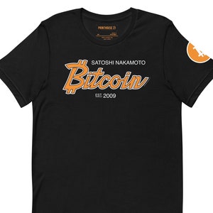 Puede incluir: Camiseta negra con un logotipo de Bitcoin naranja y el texto "Satoshi Nakamoto Bitcoin Est. 2009". La camiseta tiene un pequeño logotipo de Bitcoin naranja en la manga derecha.