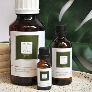 Könnte beinhalten: Drei Glasflaschen mit ätherischem Öl mit braunem Glas und schwarzen Kappen. Die Flaschen sind mit dem Text "Terra di Cera" und den Kontaktdaten des Unternehmens beschriftet. Die Flaschen stehen auf einer weiß-braunen, gefleckten Oberfläche.