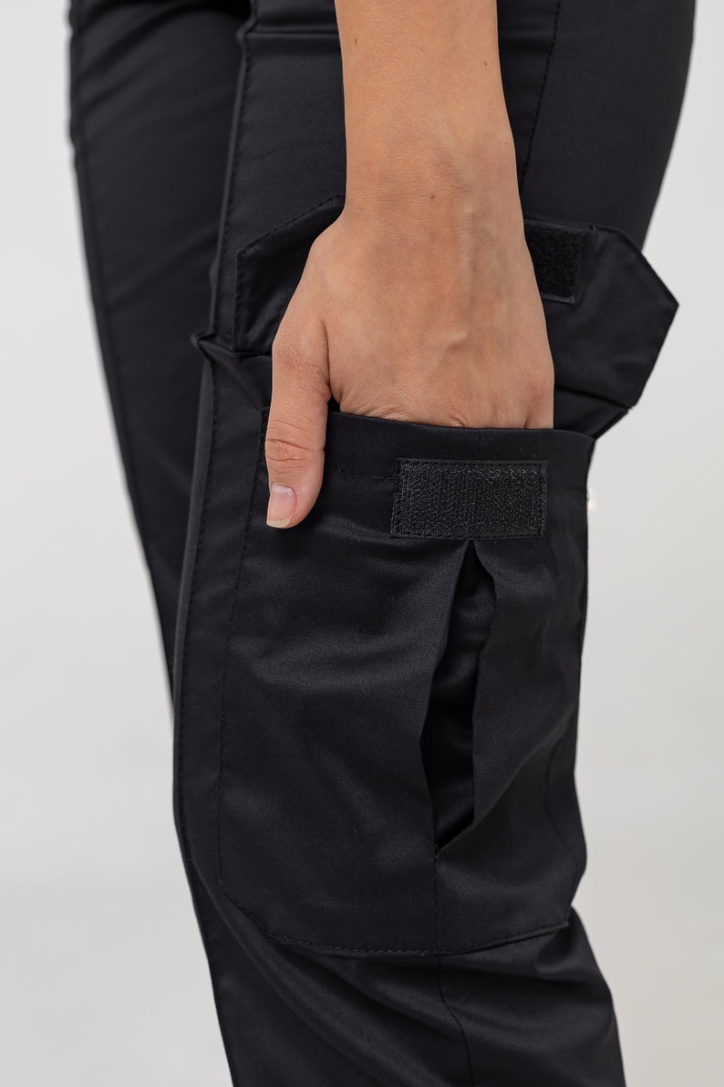 May include: Black cargo pants with a large flap pocket on the right leg. The pocket has a velcro closure.