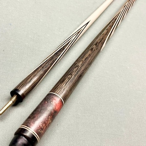 May include: Two wooden pool cues with a brown and white striped design. One cue has a red and white tip, while the other has a white tip.