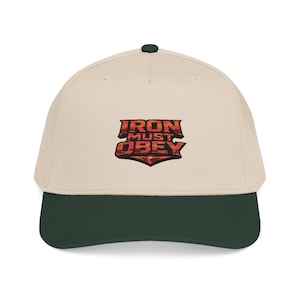 May include: A beige baseball cap with a dark green brim and a dark green button on top. The cap features the text "IRON MUST OBEY" in a red and black design.