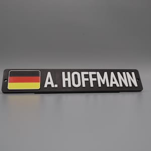 A single sign on a stand for display purposes, in with a grey background. The sign has the flag of germany on the left side, followed by the text "A. HOFFMANN".