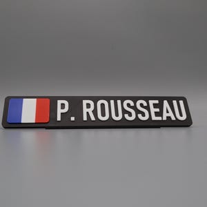 A single sign on a stand for display purposes, in with a grey background. The sign has the flag of france on the left side, followed by the text "P. ROUSSEAU".