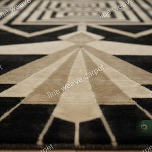 Pu&ograve; includere: Tappeto a motivi geometrici in nero, beige e marrone chiaro. Il tappeto presenta un motivo Art D&eacute;co ripetuto con linee radiali e forme angolari. La trama del tappeto &egrave; visibile, suggerendo un materiale morbido e tessuto. Le parole "fine weave carpet" sono stampate sul tappeto.