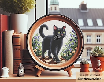 May include: A circular wooden frame containing a cross-stitch embroidery of a black cat standing on a path surrounded by purple and yellow flowers. The frame rests on a small wooden stand. Text on the image reads: All rights reserved @MyBraveStitch Hanna Levchuk.