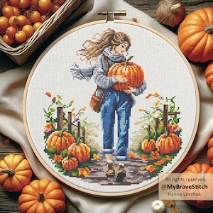 May include: Cross-stitch embroidery in a wooden hoop depicts a person carrying a large orange pumpkin. The person is wearing blue jeans, a gray jacket, and a scarf. Pumpkins and foliage surround the person. The text "All rights reserved @MyBraveStitch Hanna Levchuk" is in the lower right corner.