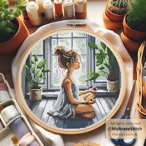 May include: A cross-stitch embroidery hoop featuring a woman meditating in front of a window, surrounded by potted plants. The design is in shades of gray, blue, and brown, with a wooden hoop. The text "All rights reserved @MyBraveStitch Hanna Levchuk" is visible.