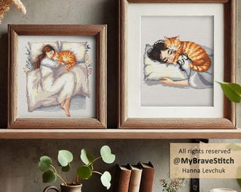 May include: Two framed cross-stitch artworks featuring illustrations of a person sleeping with an orange tabby cat. The left frame shows a full-body view, while the right frame shows a close-up of the person and cat resting on a pillow.