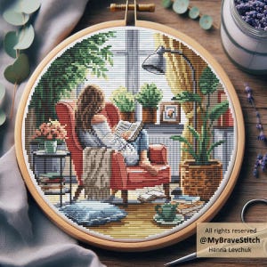 Op de afbeelding: Een kruissteek borduurring met een gezellige leesscène. Het ontwerp toont een persoon in een rode fauteuil die leest, omringd door planten, een lamp en een raam. De tekst "All rights reserved @MyBraveStitch Hanna Levchuk" is zichtbaar.