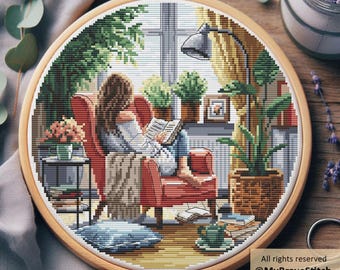 May include: A cross-stitch embroidery hoop showing a person reading in a room filled with plants. The scene includes a red armchair, a window, and a lamp. The text "All rights reserved @MyBraveStitch Hanna Levchuk" is visible on the design.