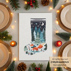 Op de afbeelding: Een kruissteekontwerp van een kerstsok met een winterbosscène en een vos. De sok is gevuld met groenblijvende bomen, sneeuwvlokken en een halve maan. Het woord "CHRISTMAS" is bovenaan gestikt. Het kunstwerk wordt op een wit canvas getoond.