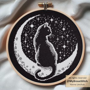 May include: Cross-stitch embroidery in a wooden hoop. The design shows a black cat on a crescent moon against a starry night sky. The text "All rights reserved @MyBraveStitch Hanna Levchuk" is visible.