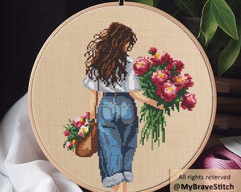 Puede incluir: Bordado de punto de cruz de una persona sosteniendo un ramo de peonías rojas y una cesta de flores. La persona lleva una camisa blanca y vaqueros azules. El bordado está en un aro de madera. El texto dice: "All rights reserved @MyBraveStitch Hanna Levchuk."