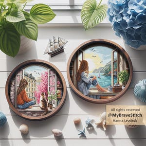 Op de afbeelding: Twee ronde, ingelijste kruissteekkunstwerken tonen serene scènes. Eén toont een persoon die uit een raam kijkt naar een Europese straat, de andere naar een kustzicht. Een kleine zeilboot en diverse schelpen sieren het witte oppervlak. De tekst "All rights reserved @MyBraveStitch Hanna Levchuk" is zichtbaar.