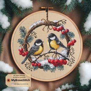 Peut inclure: Un cerceau de broderie en point de croix représentant deux oiseaux à poitrine jaune perchés sur une branche d'hiver avec des baies rouges. Le cerceau est entouré d'un cadre en bois brun.