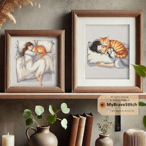 May include: Two framed cross-stitch artworks show a person sleeping with a ginger cat. The artwork on the left shows a person in bed with a cat. The artwork on the right shows a close-up of a person and a cat. Both are in wooden frames.